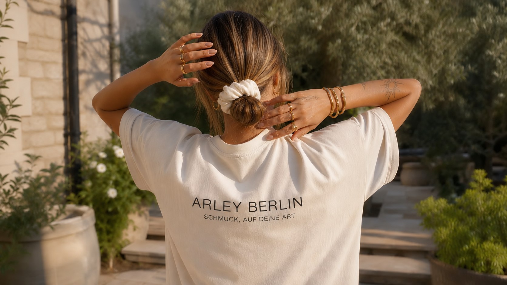 Frau in einem Arley-Berlin-T-Shirt mit goldenem Schmuck in einem Garten