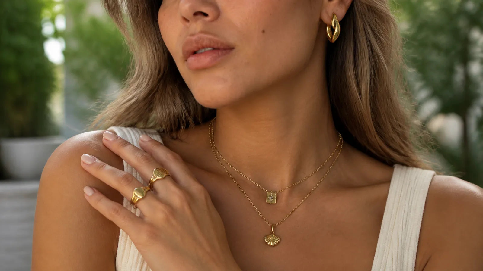 Woman layering Arley London gold rings, necklaces and earrings in a garden setting
