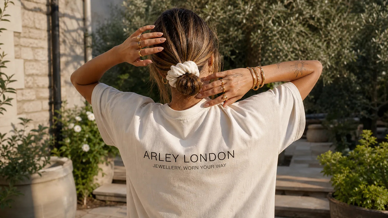 Woman in an Arley London T-shirt styling gold jewellery in an English garden